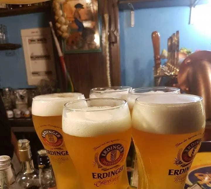 Quattro bicchieri alti di birra di frumento appena spillata, sul bancone di legno davanti alle pareti azzurre