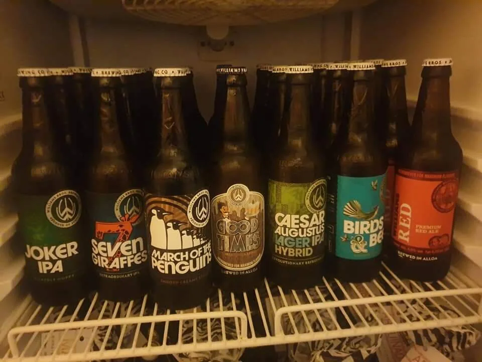 Una fila di bottiglie di birra artigianale allineate su un ripiano del frigorifero del pub