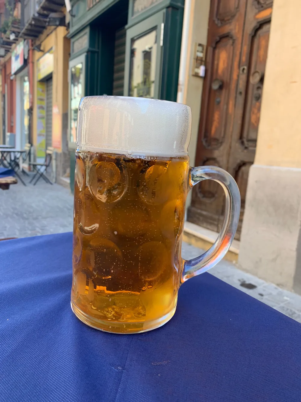 Un boccale di birra da un litro pieno, appoggiato sulla tovaglia blu di un tavolo davanti al pub