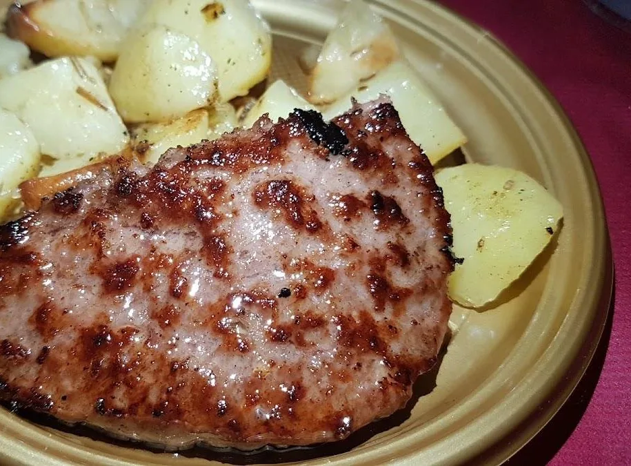 Una fetta di carne alla griglia con patate al forno servita in un piatto, sul tavolo del pub