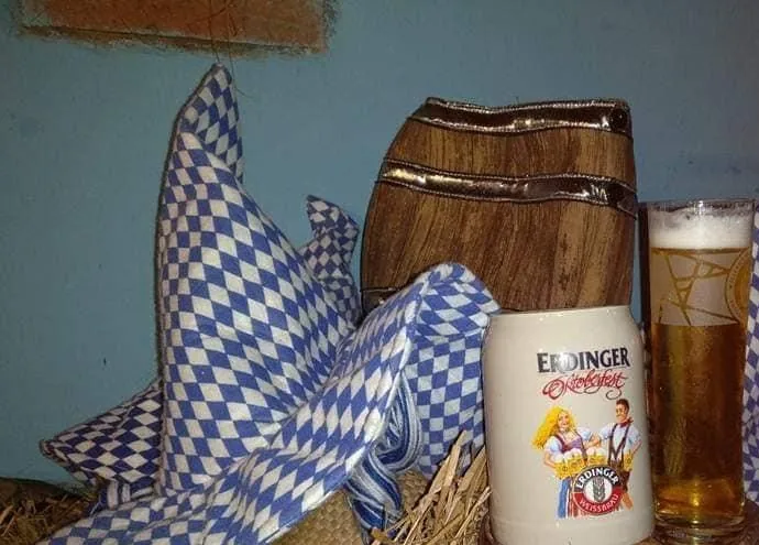 Boccale di ceramica appoggiato su una botte, con stoffe a rombi bianchi e blu e paglia dietro