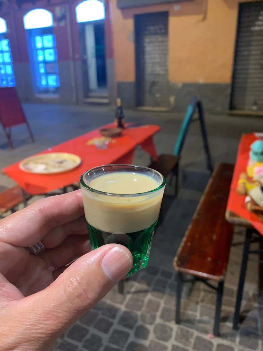 Uno shot tenuto in mano davanti ai tavoli rossi del pub, di sera, sul selciato del Corso