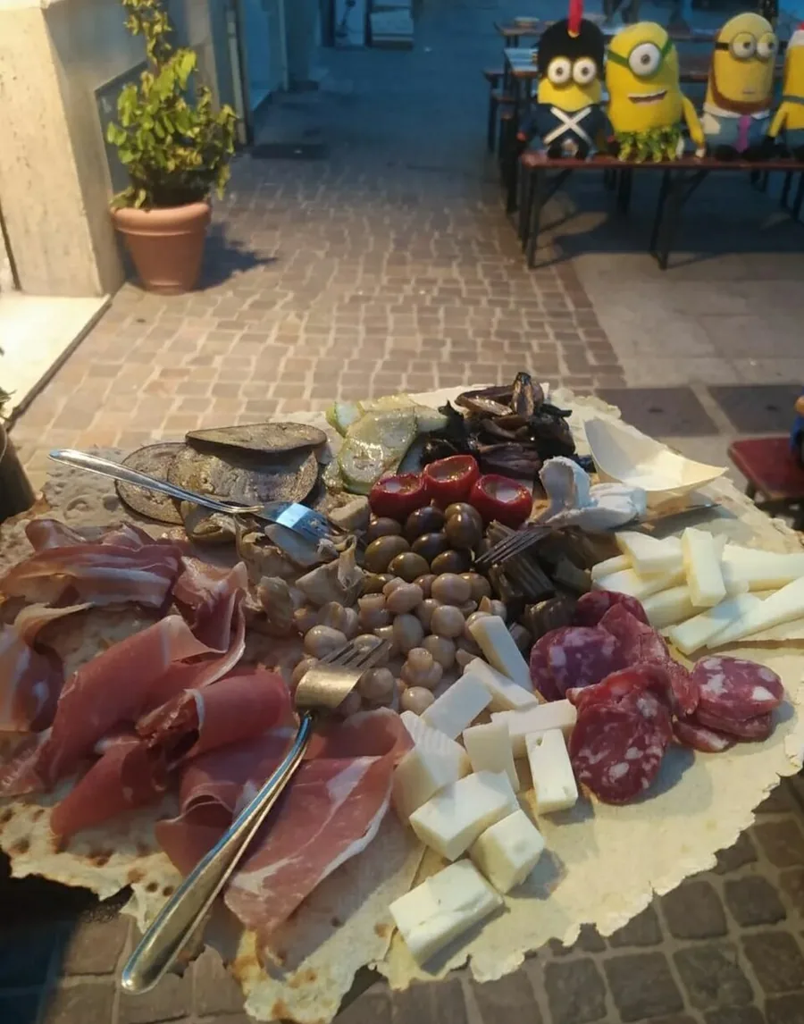 Un tagliere servito sul pane carasau: prosciutto crudo, salame, cubetti e scaglie di pecorino, olive, funghetti sott'olio e verdure grigliate